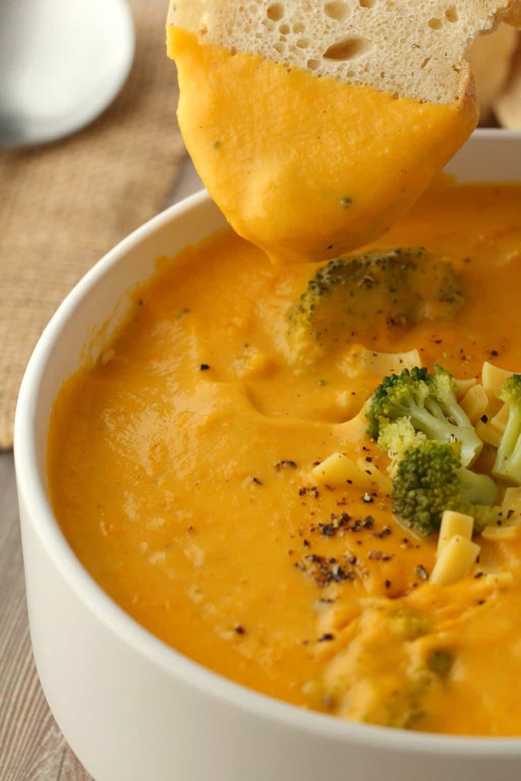 Slice of bread dipping into a bowl of vegan broccoli cheese soup.