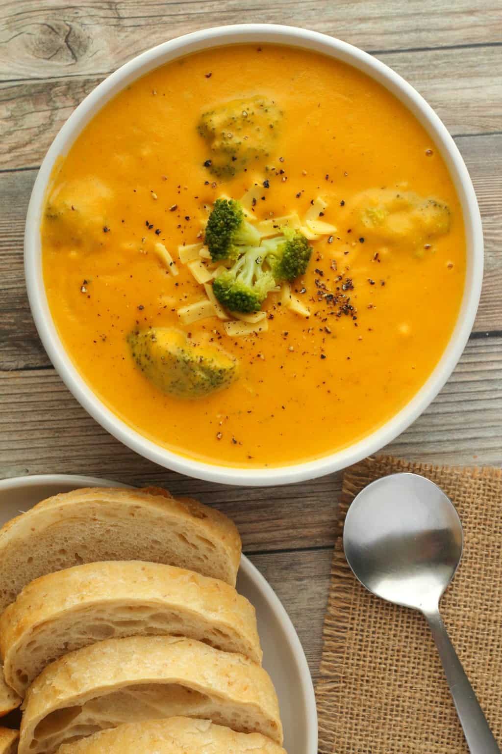 Vegan broccoli cheese soup topped with broccoli pieces and grated cheese in a white bowl. 