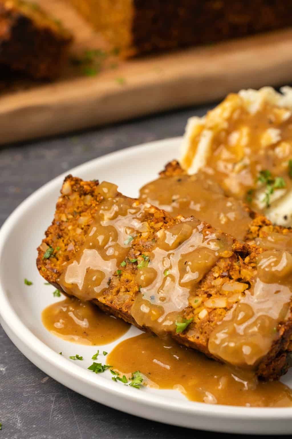 Slices of vegan nut roast drizzled with gravy on a white plate. 