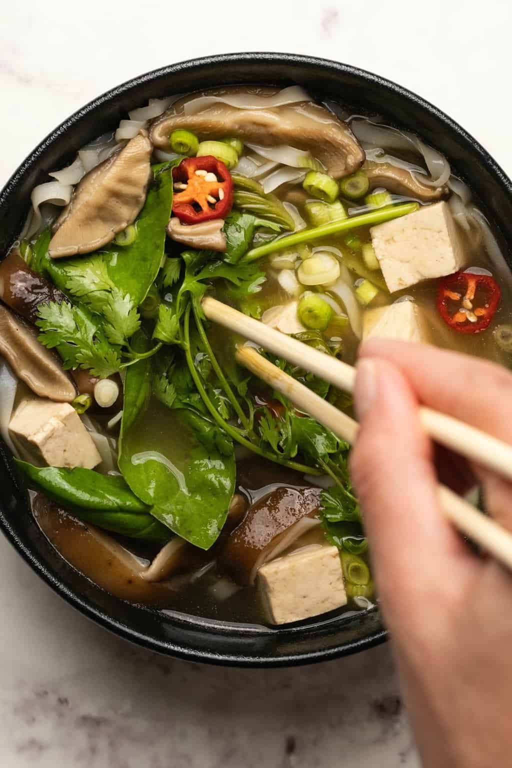 Vegan pho in a black bowl with chopsticks. 