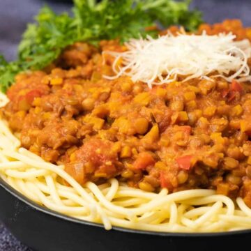 Lentil bolognese with spaghetti and vegan parmesan in a black bowl.