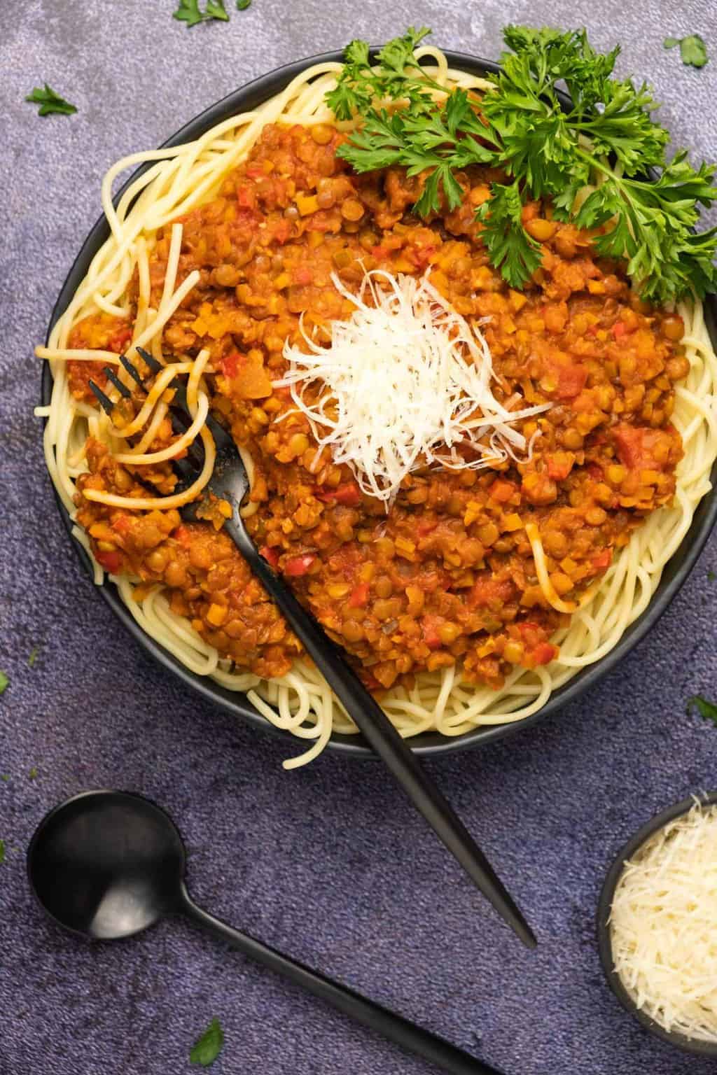 Lentil bolognese with spaghetti and vegan parmesan in a black bowl. 