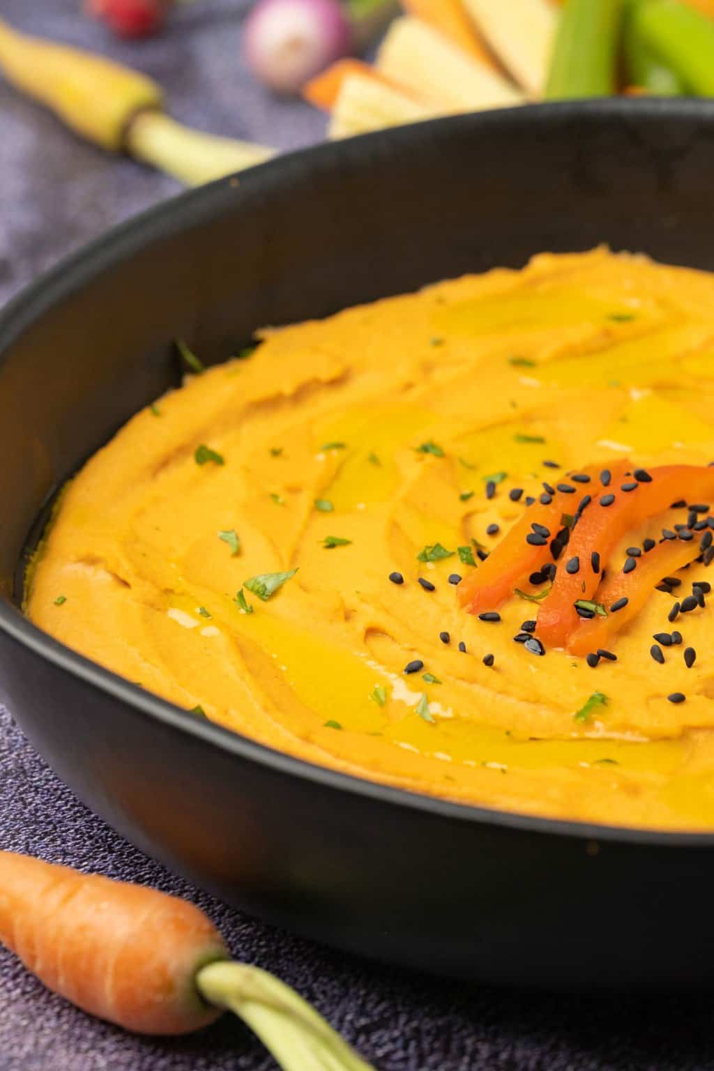 Roasted red pepper hummus topped with sesame seeds in a black bowl. 