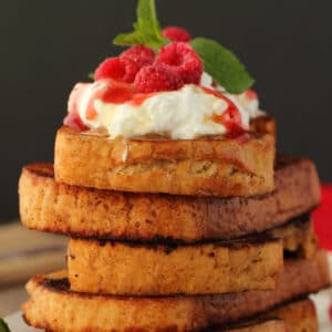Vegan french toast in a stack topped with vegan whipped cream and raspberries.