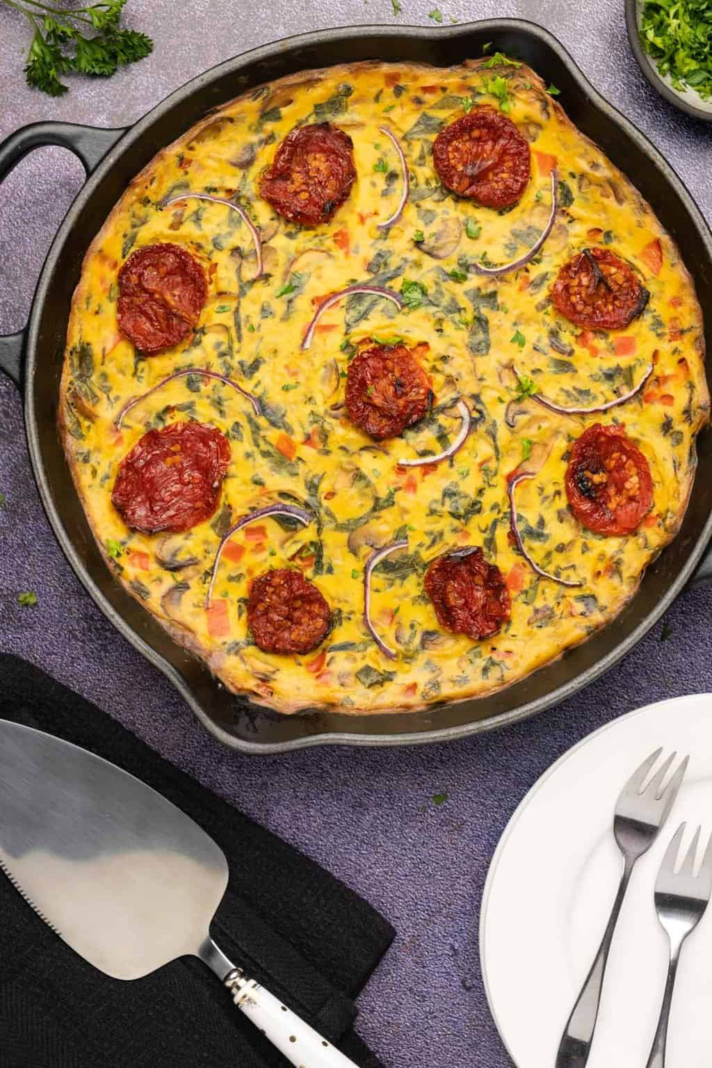 Vegan frittata topped with sundried tomato and red onion in a cast iron skillet. 