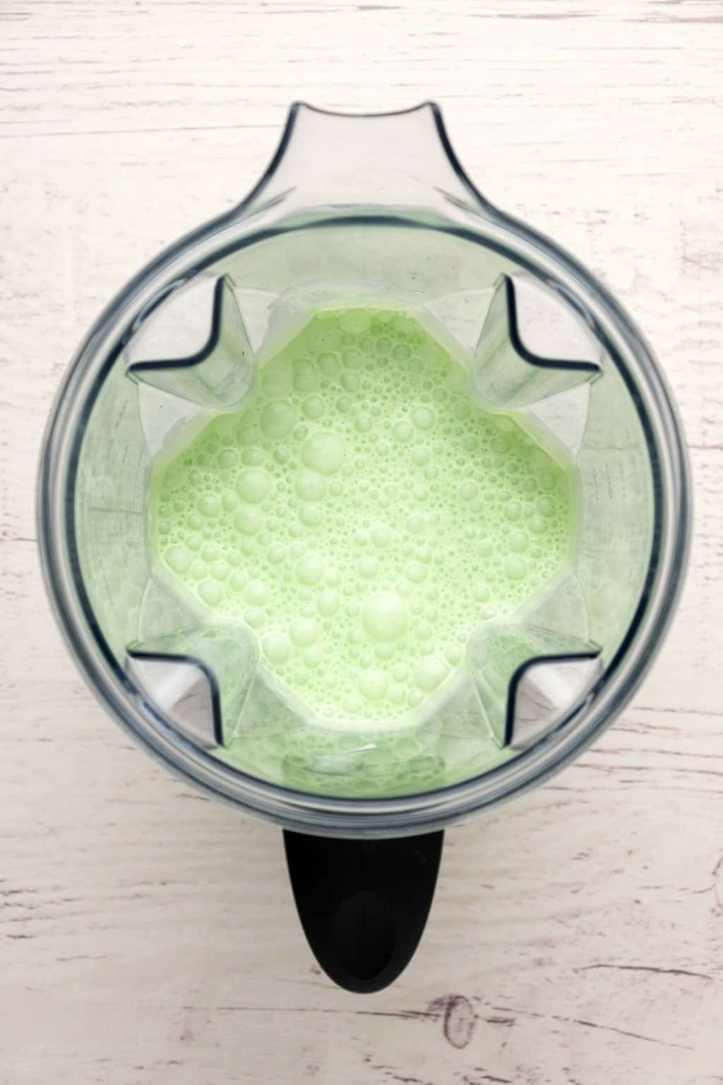 Blender jug with freshly blended mint green milkshake. 