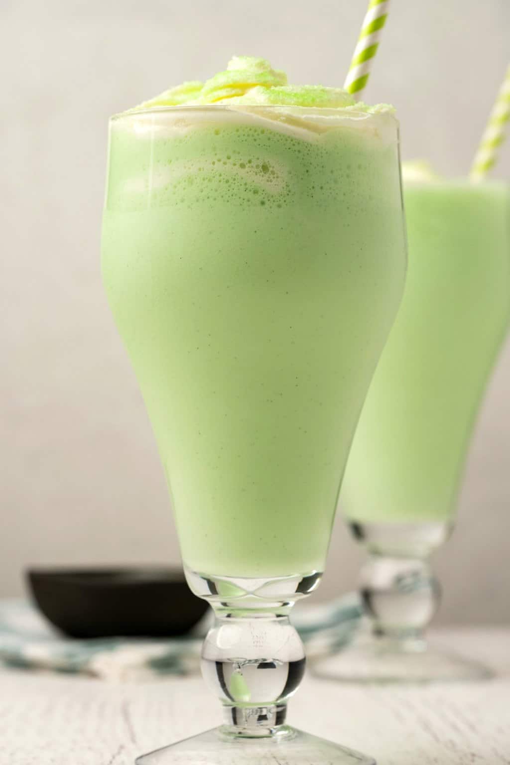 Vegan shamrock shakes in tall glasses with green and white striped straws. 