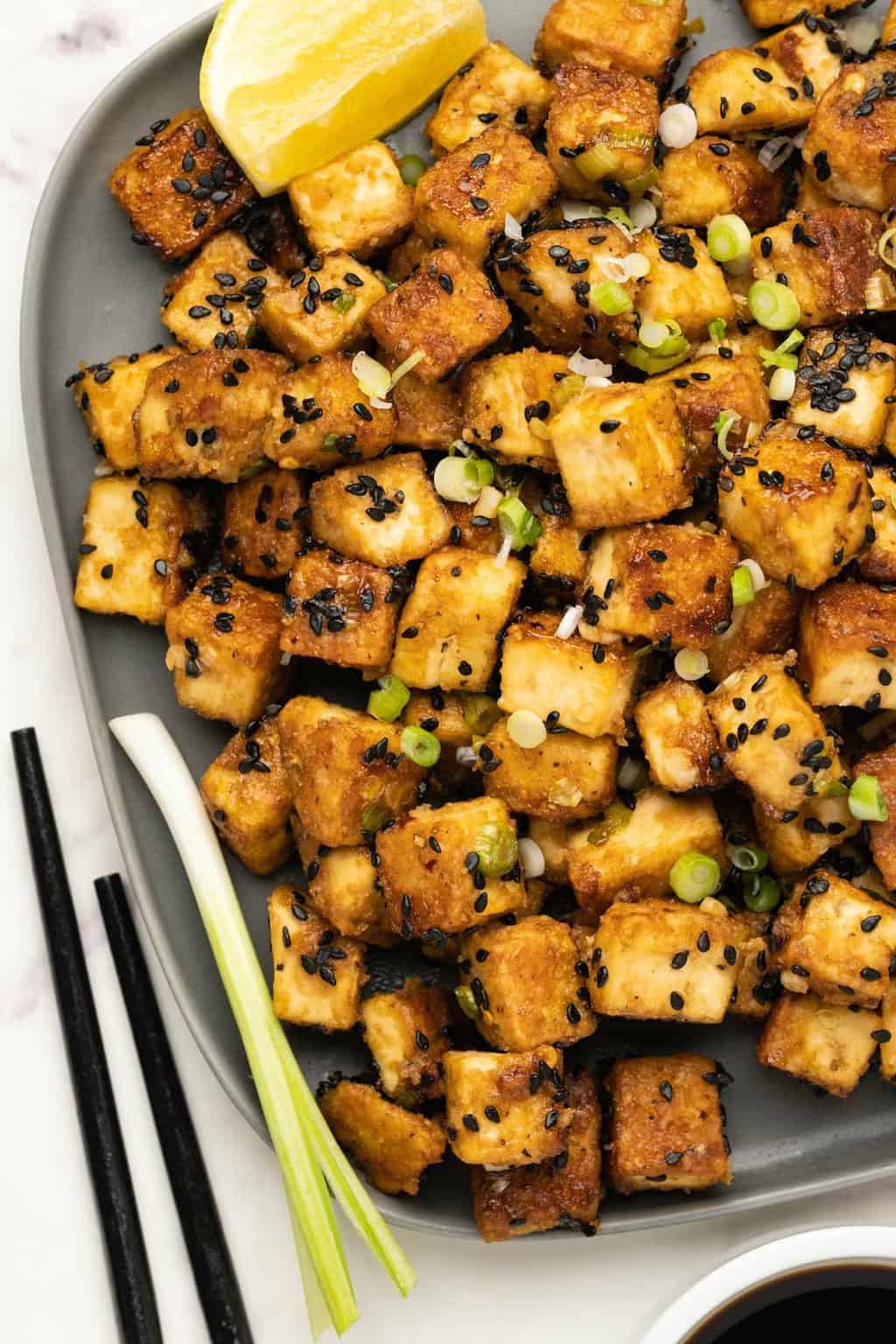 Fried Tofu with spring onions and black sesame seeds on a gray plate. 