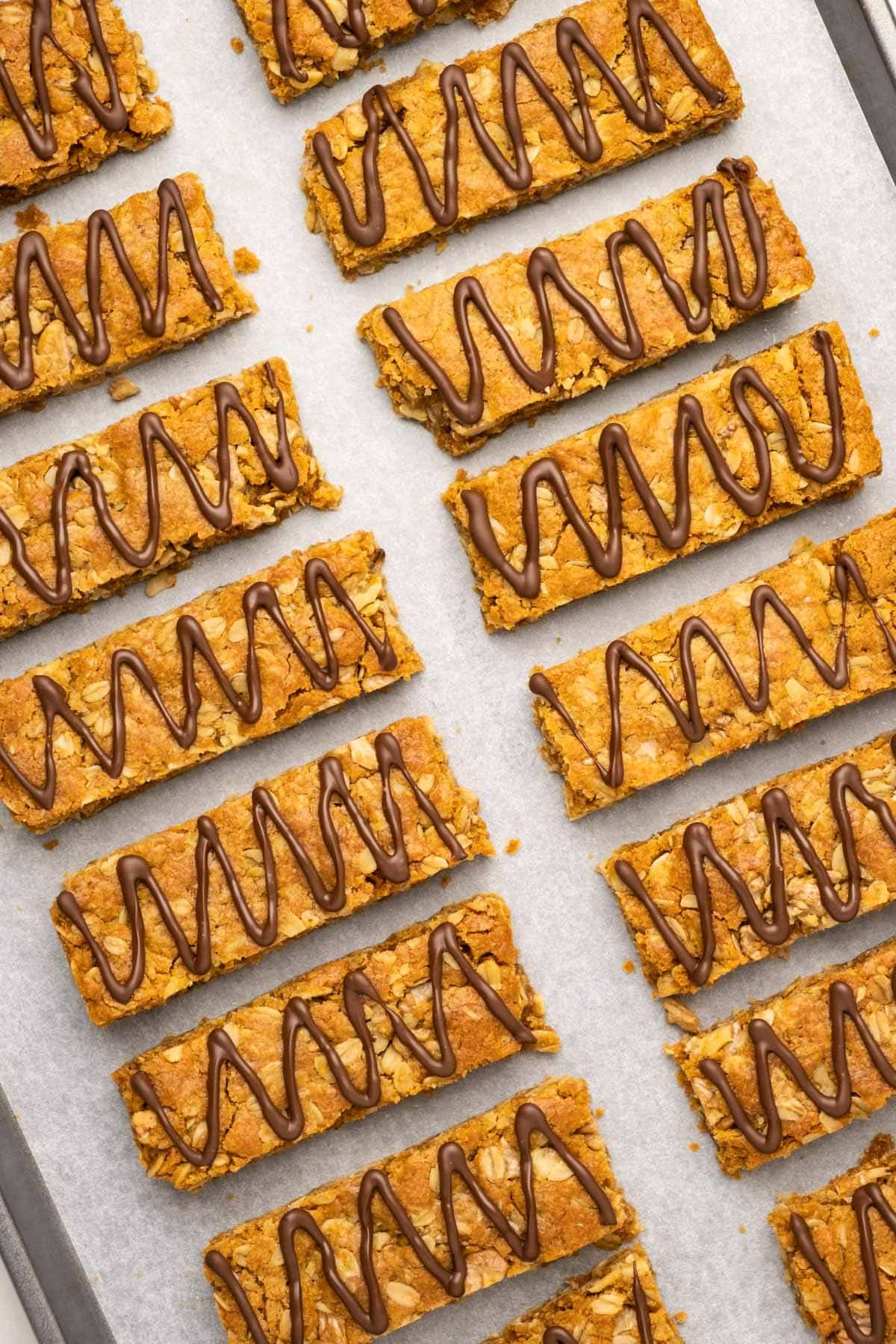 Vegan oatmeal bars drizzled with chocolate on a parchment lined baking sheet.