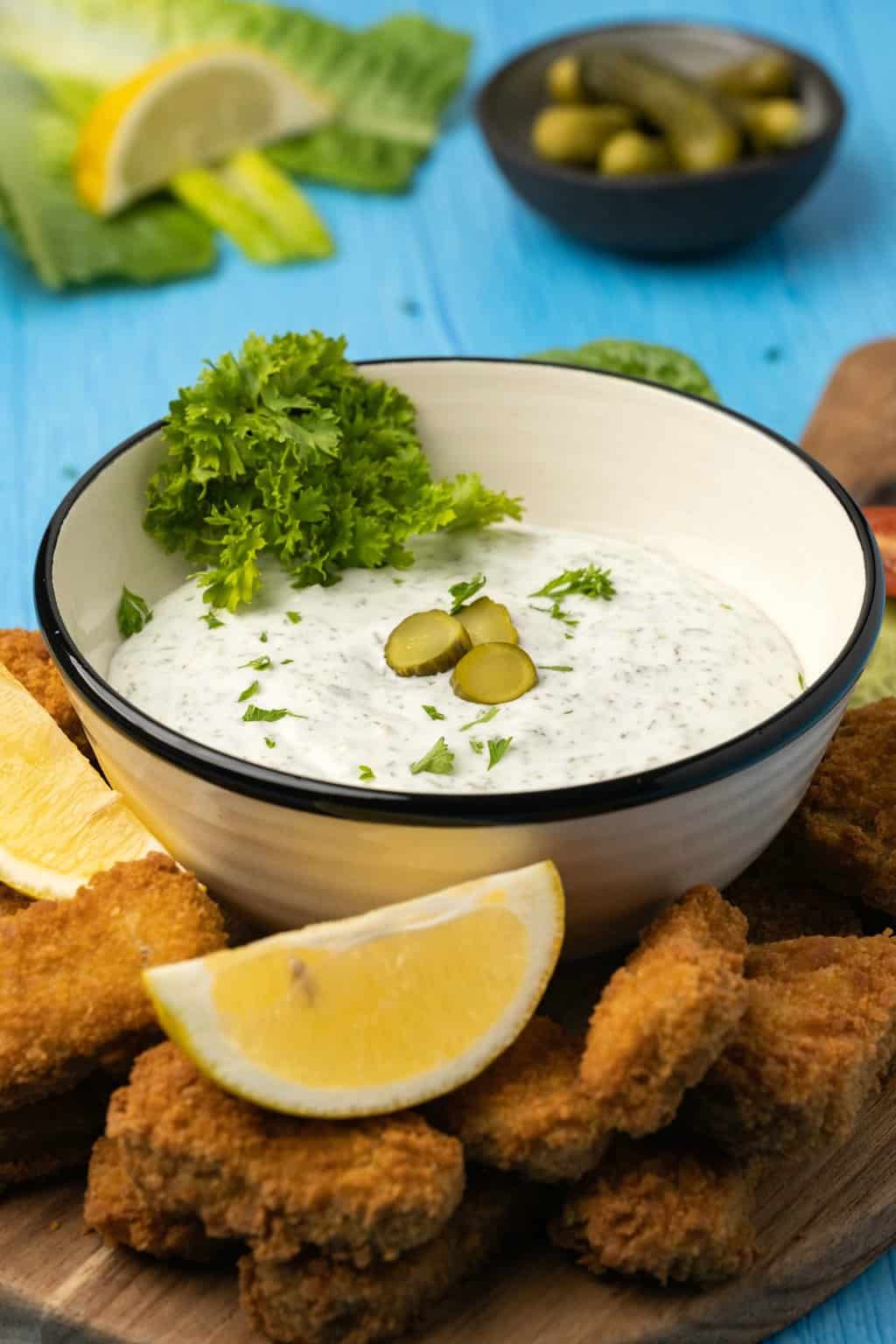 Vegan tartar sauce in a ceramic bowl topped with sliced dill and fresh parsley. 