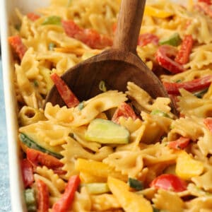 Vegan pasta salad in a white dish with a wooden serving spoon.