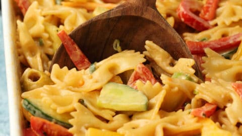 Vegan pasta salad in a white dish with a wooden serving spoon.