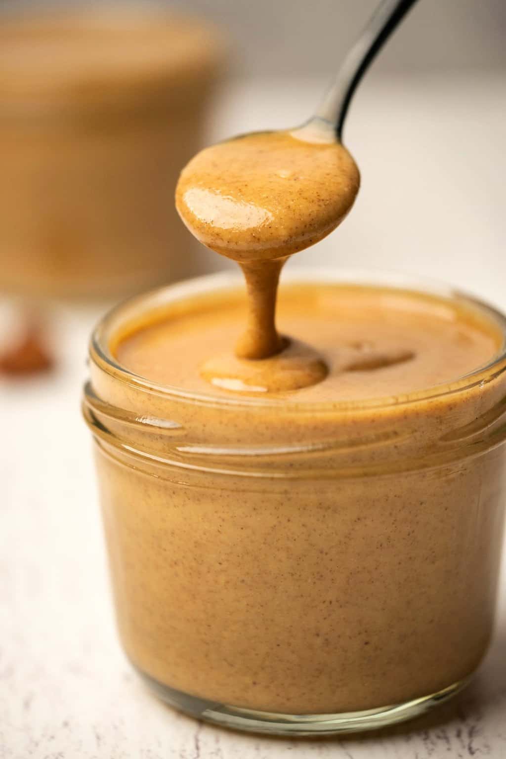 Spoonful of almond butter above a glass jar. 