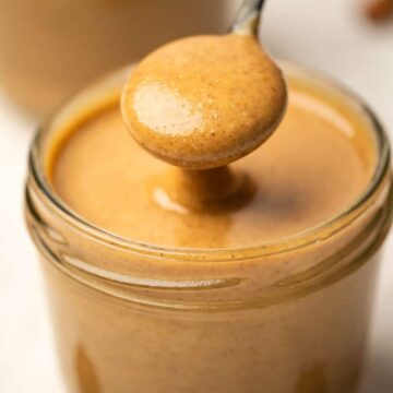 Almond butter in a glass jar with a spoon.