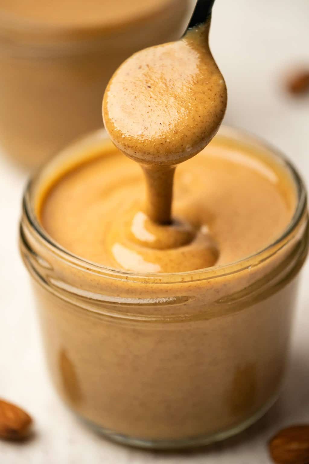 Almond butter in a glass jar with a spoon. 