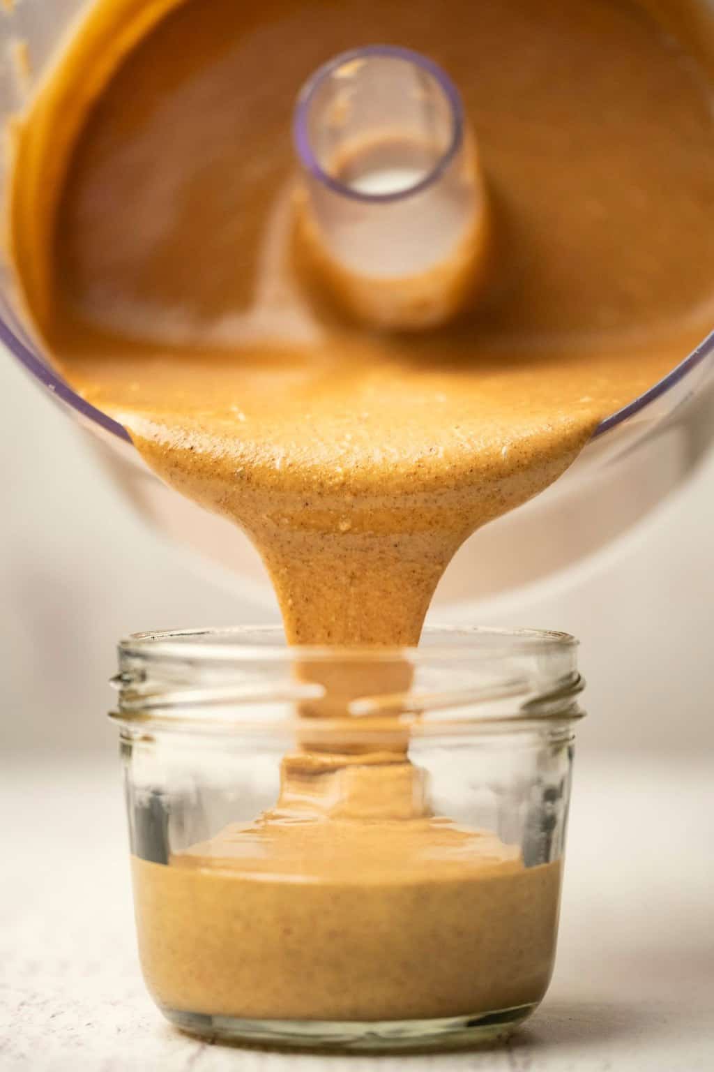 Almond butter pouring from a food processor into a glass jar. 
