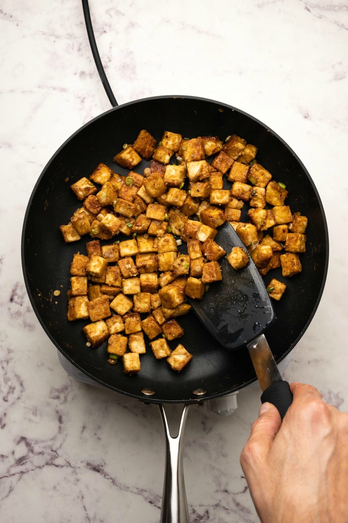 Fried tofu in a pan with a spatula.