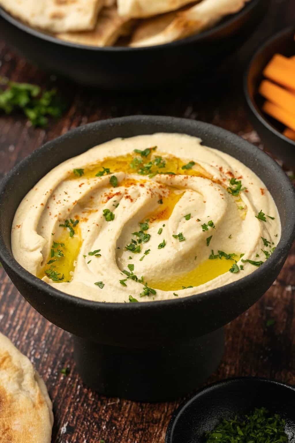 Hummus topped with fresh parsley, paprika and olive oil in a black bowl. 