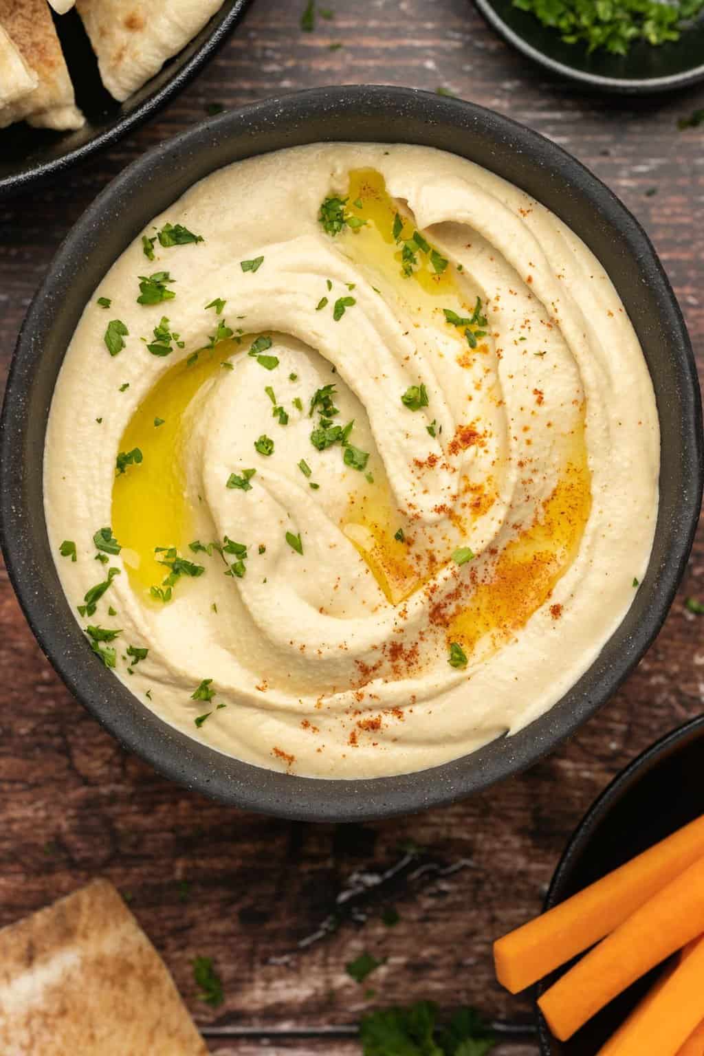 Hummus with paprika, olive oil and fresh parsley in a black bowl. 