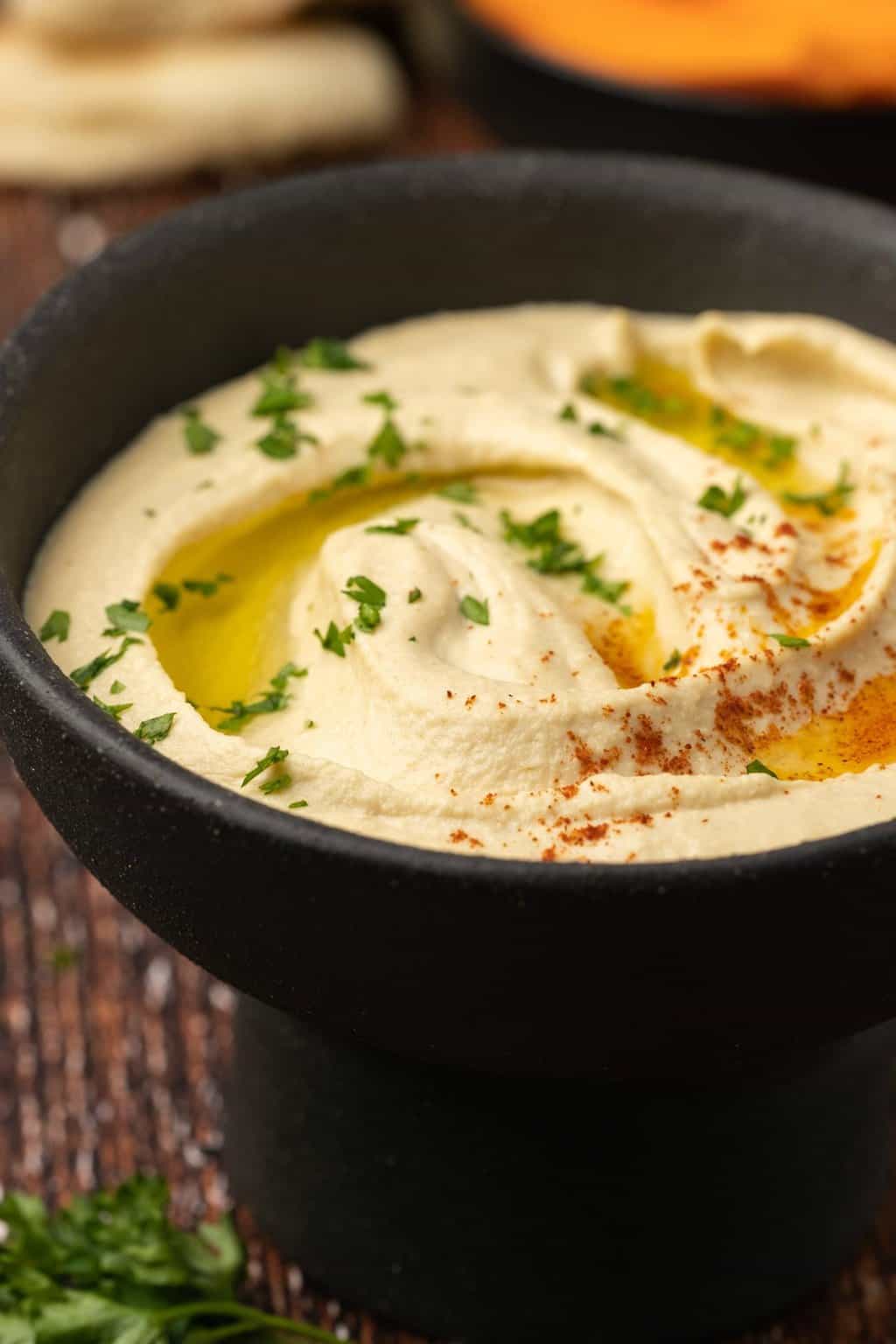 Hummus in a black bowl with fresh parsley, paprika and olive oil. 