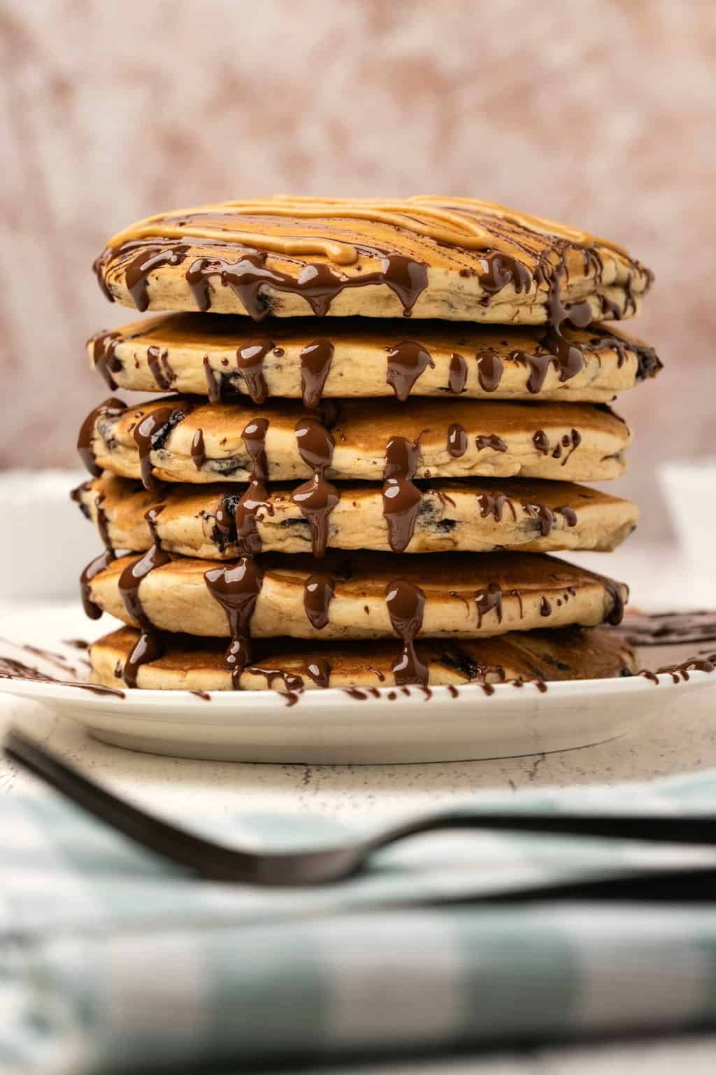 Vegan peanut butter pancakes drizzled with melted peanut butter and chocolate on a white plate. 