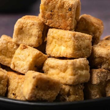 Baked tofu cubes stacked up on a black plate.