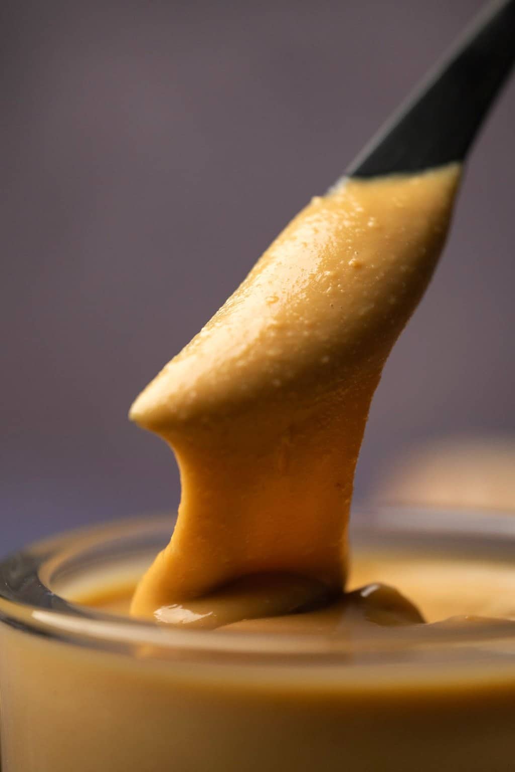 A knife dipping into a glass jar of peanut butter. 
