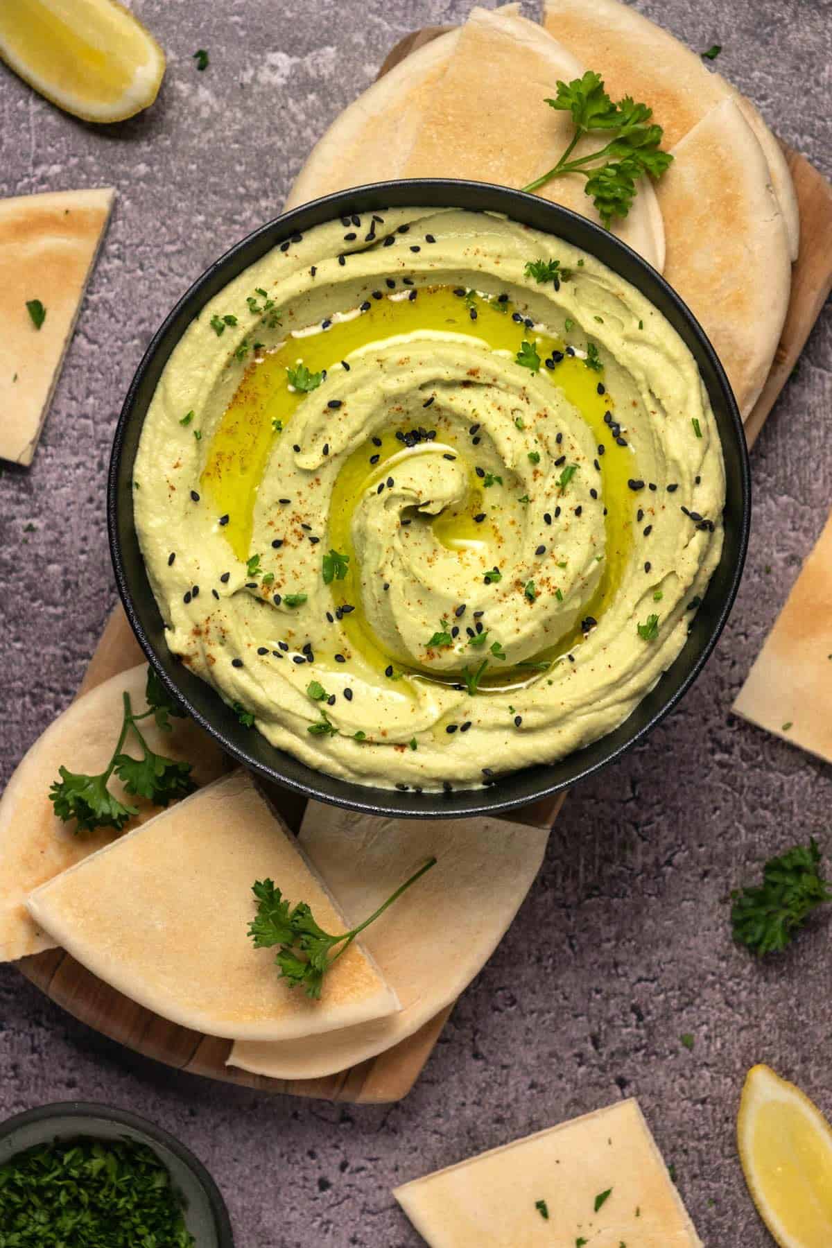 Avocado hummus topped with black sesame seeds, olive oil and chopped parsley in a black bowl. 