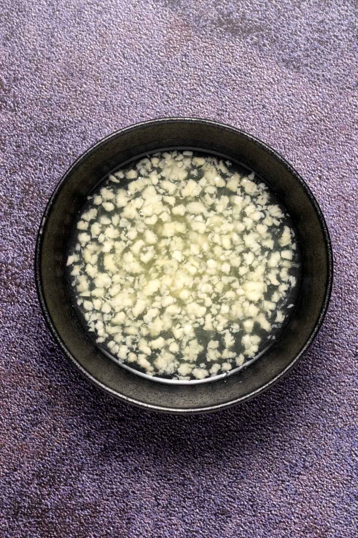 Crushed garlic soaking in fresh lemon juice in a black bowl.
