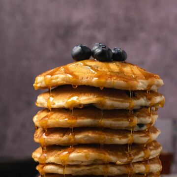 Vegan blueberry pancakes stacked up on a white plate.