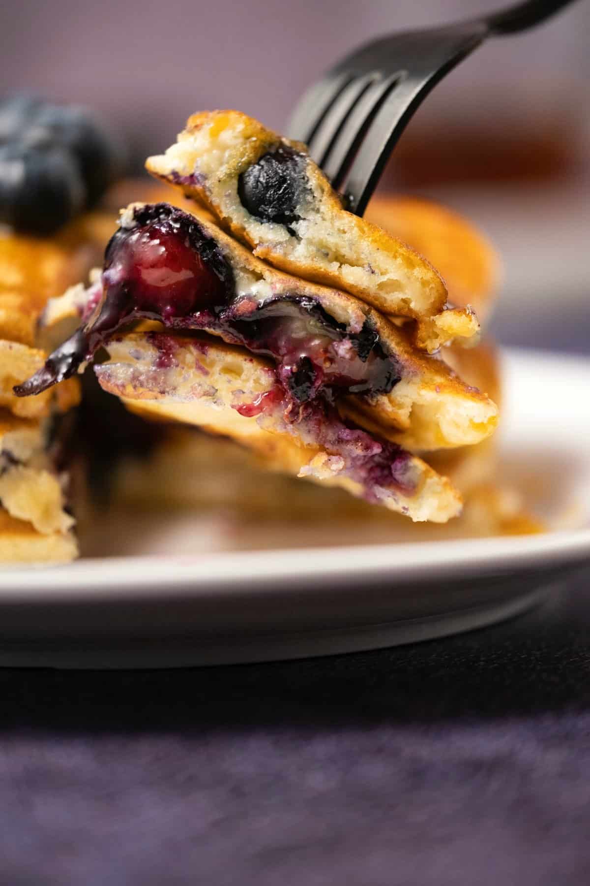 Forkful of blueberry pancakes on a white plate. 