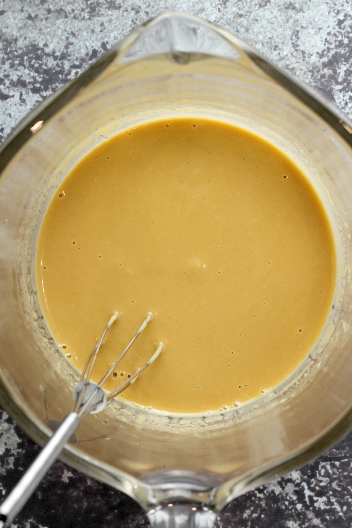 Tahini dressing in a measuring jug with a whisk.