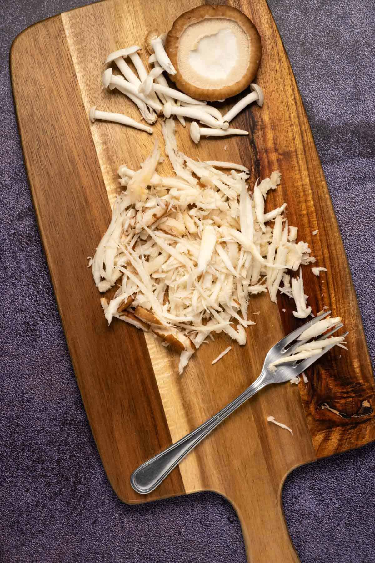 Shredded mushrooms and a fork on a wooden board. 