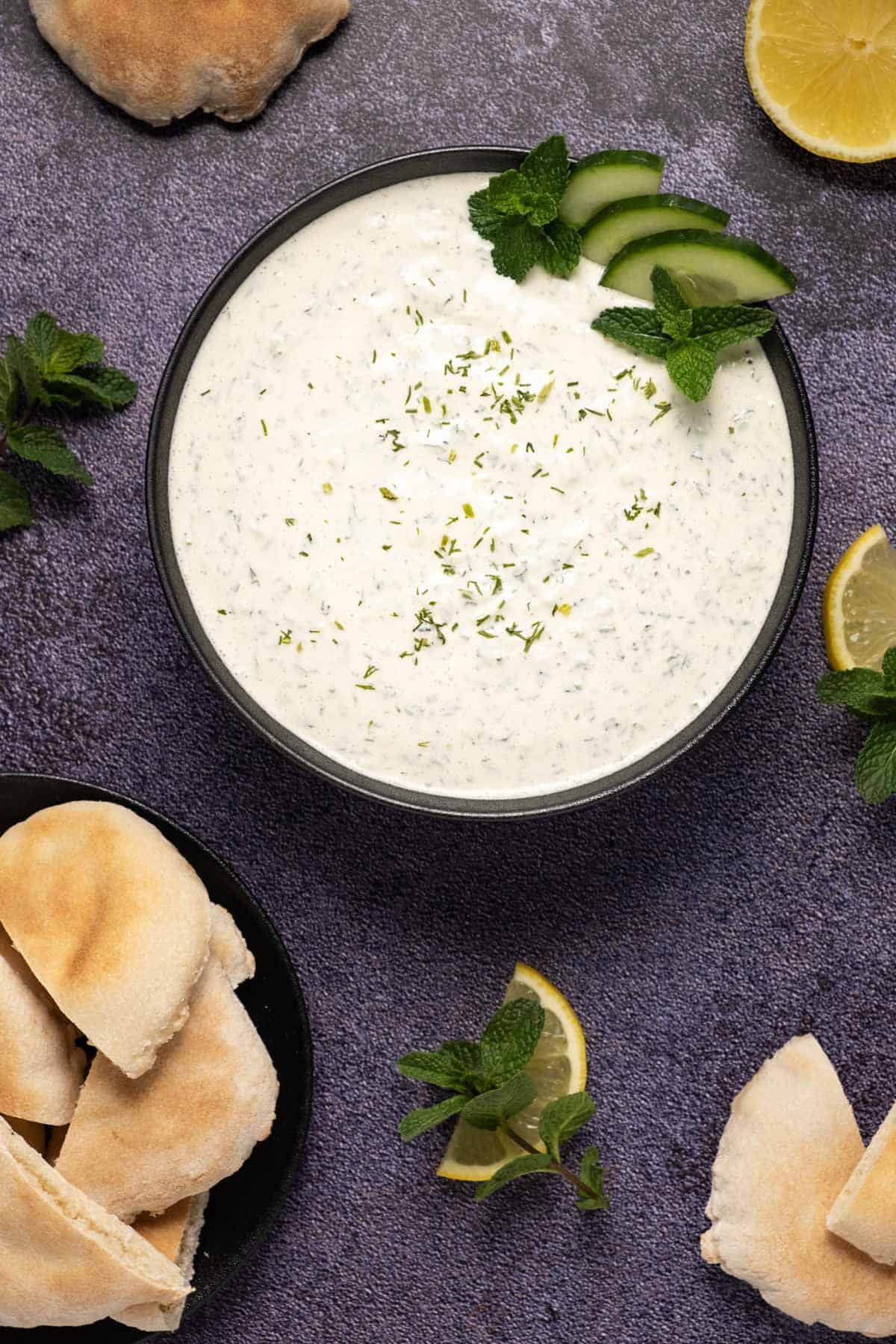 Bowl of vegan tzatziki topped with sliced cucumber, fresh mint and dried dill. 
