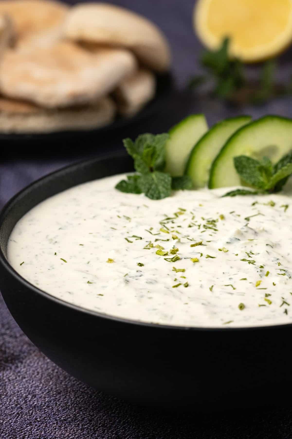 Bowl of tzatziki topped with dried dill, sliced cucumber and fresh mint. 