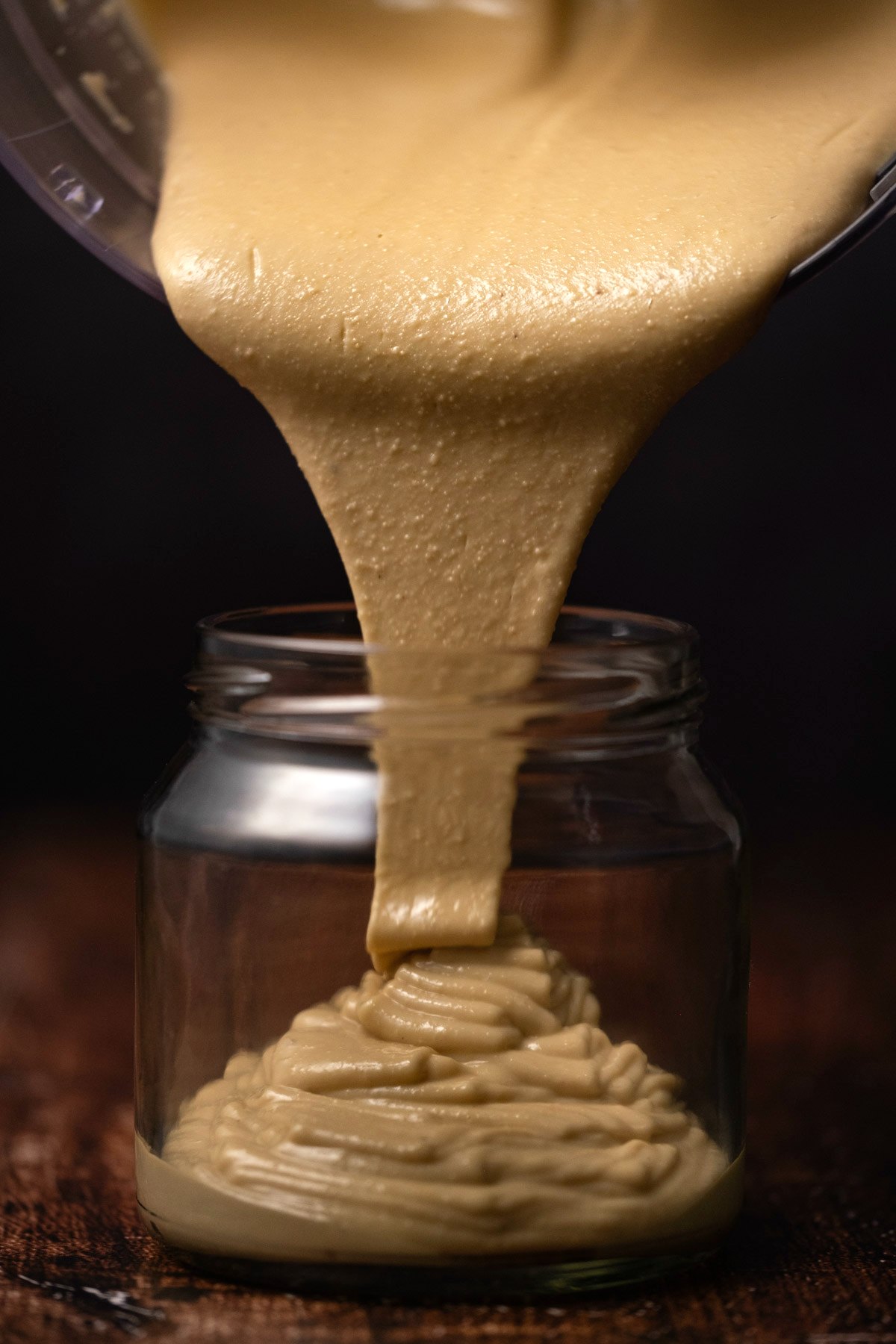 Cashew butter pouring from a food processor into a glass jar. 