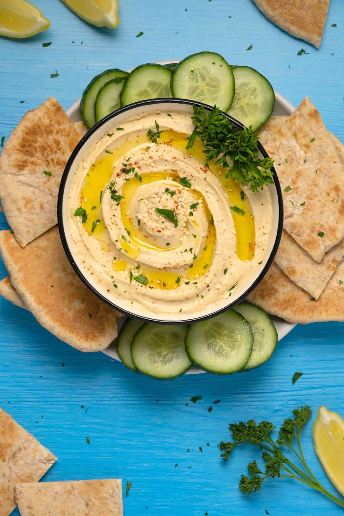 Roasted garlic hummus topped with fresh parsley, olive oil and sesame seeds in a ceramic bowl.