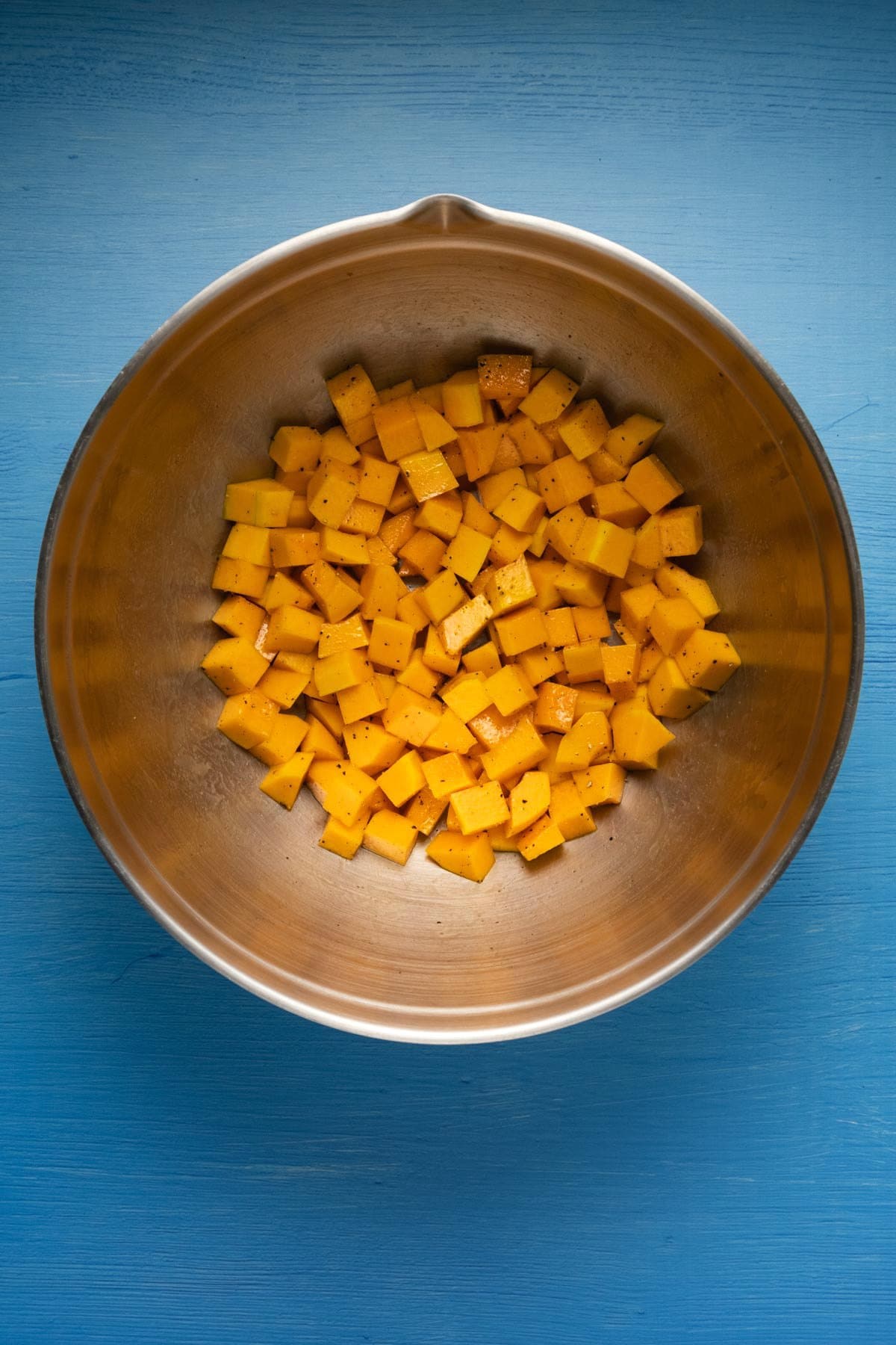 Chopped butternut squash with olive oil and spices in a mixing bowl. 