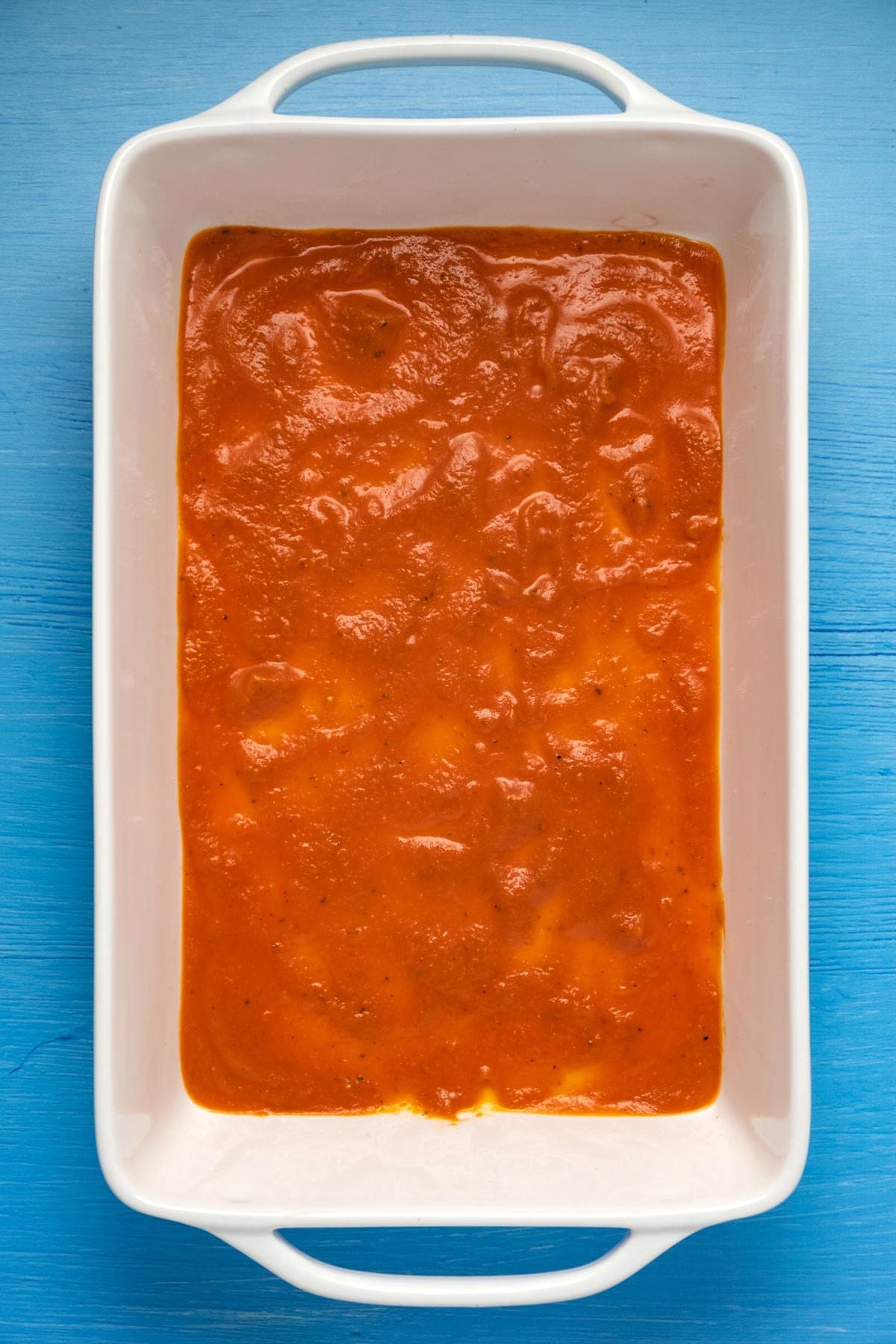 Tomato sauce at the bottom of a 9x13 white baking dish.