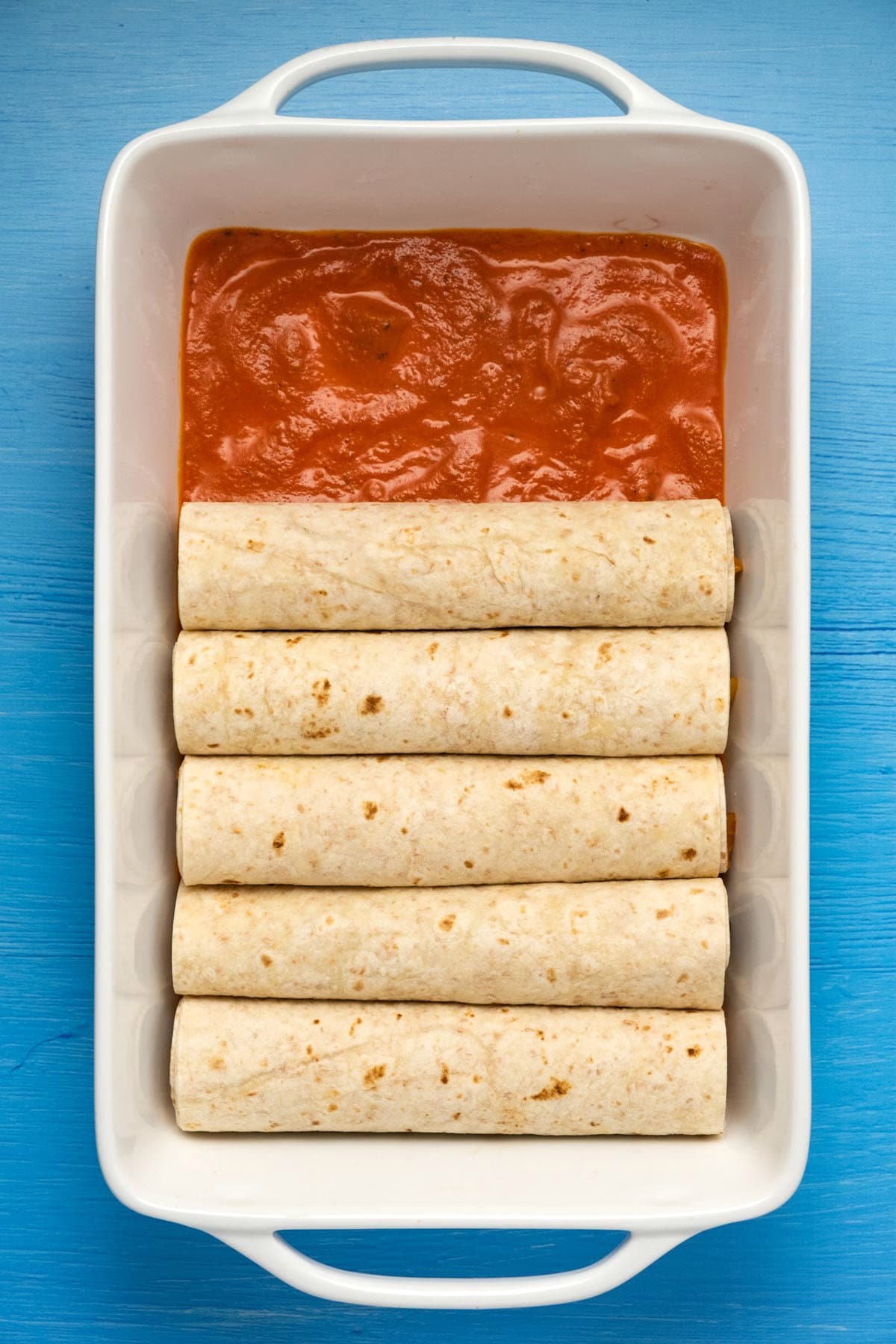Rolled tortillas in a white baking dish.