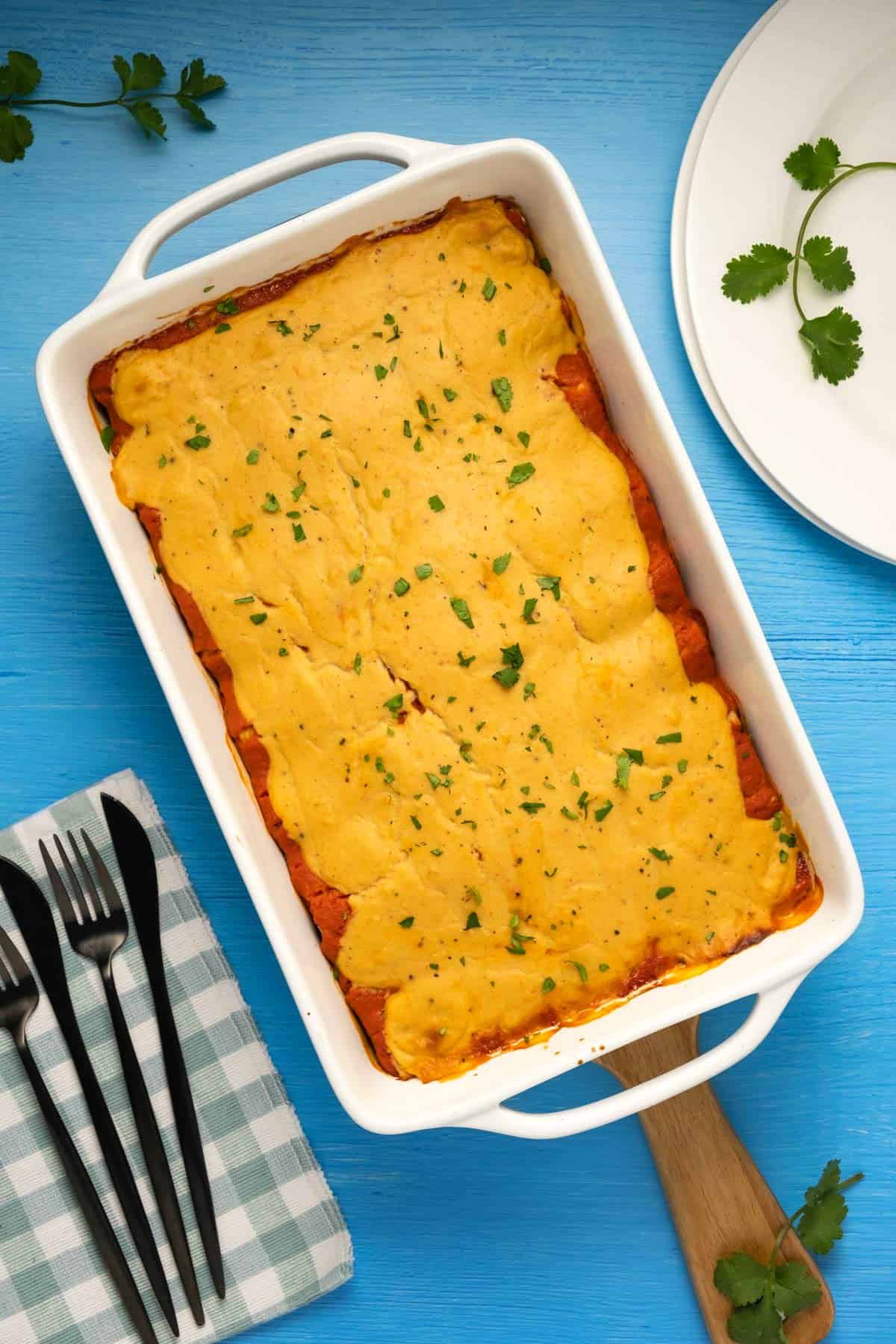 Vegan enchiladas topped with cheese sauce and chopped cilantro in a white dish. 