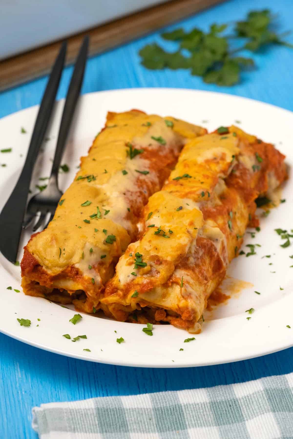 Enchiladas on a white plate with a knife and fork.