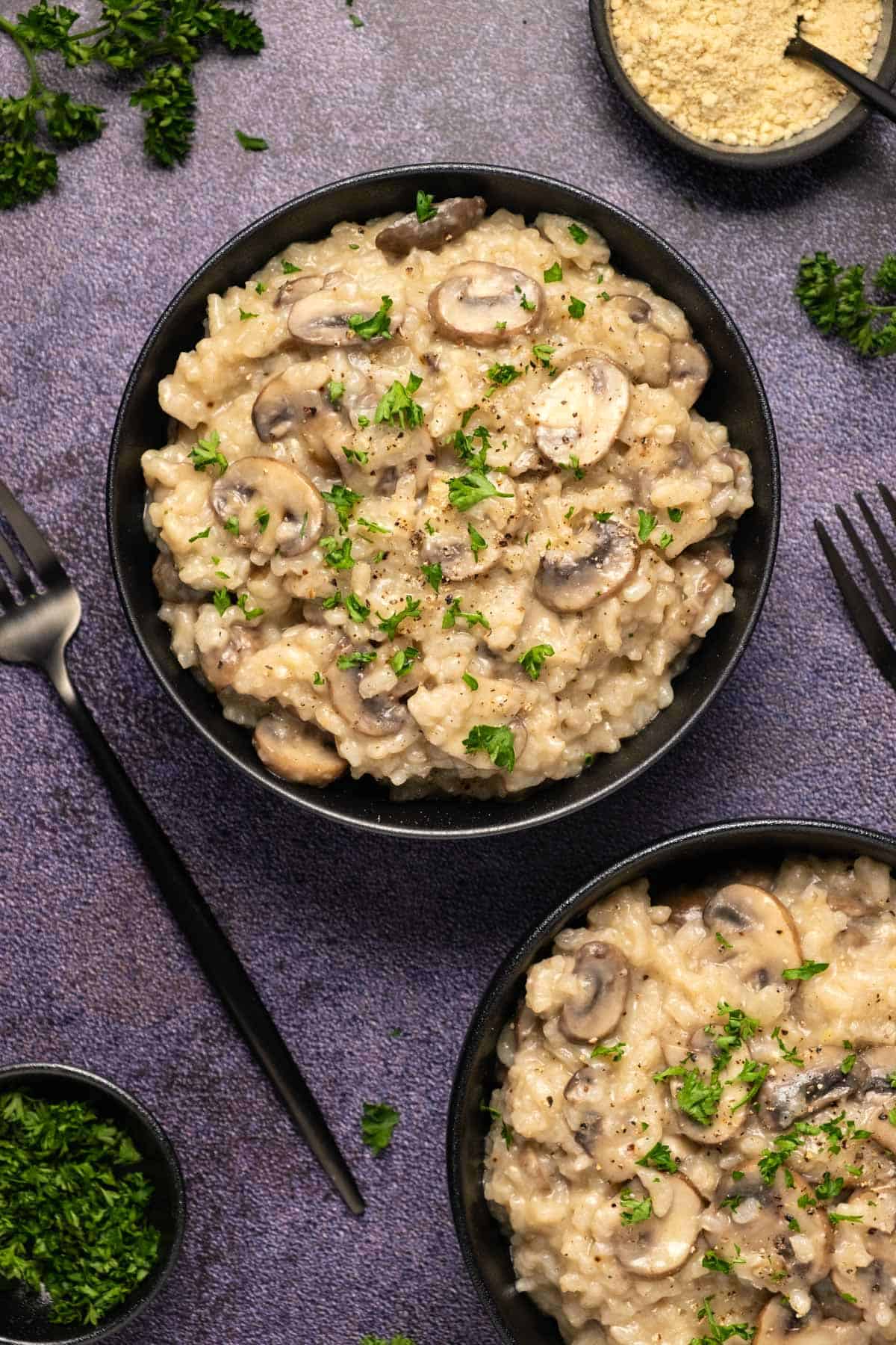 Vegan mushroom risotto topped with fresh chopped parsley and black pepper in a black bowl. 
