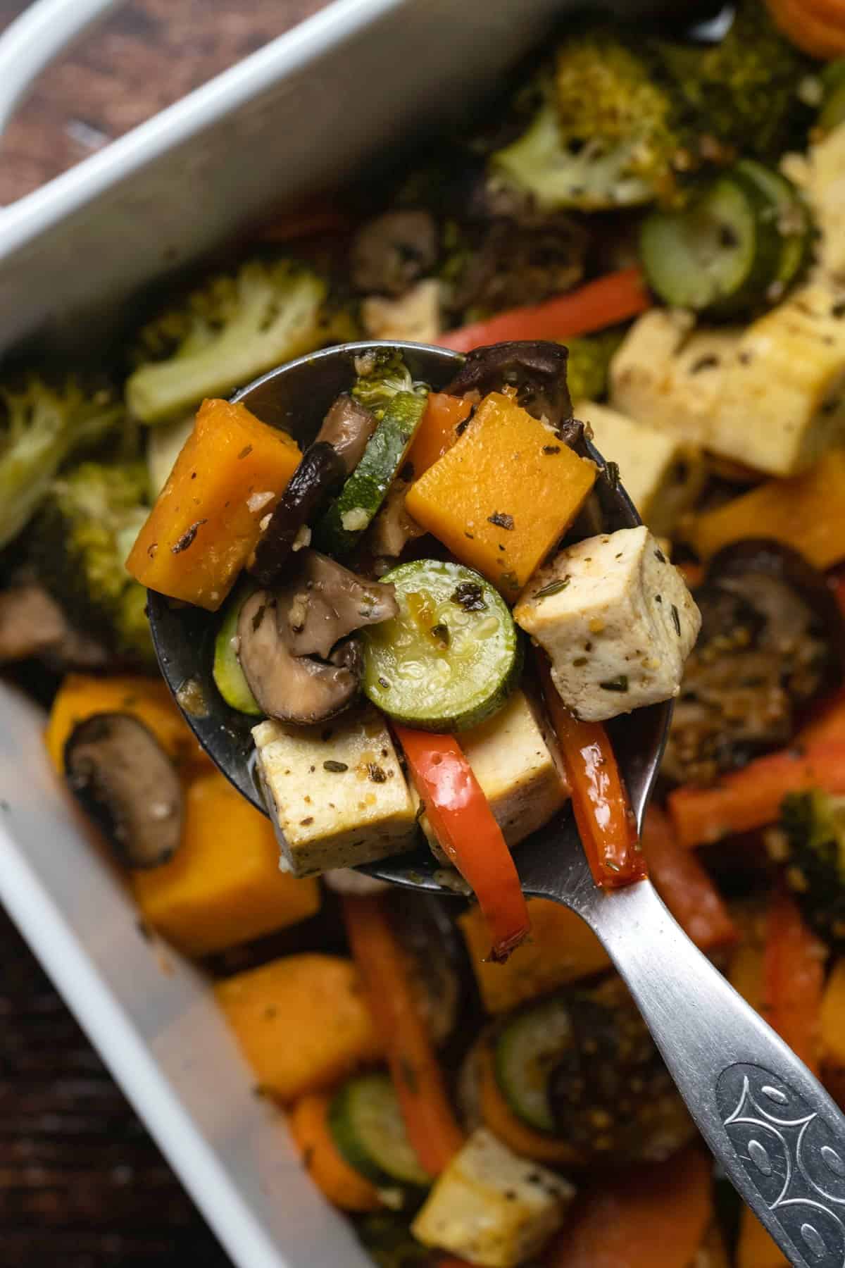 Vegetable casserole in a white baking dish with a serving spoon. 
