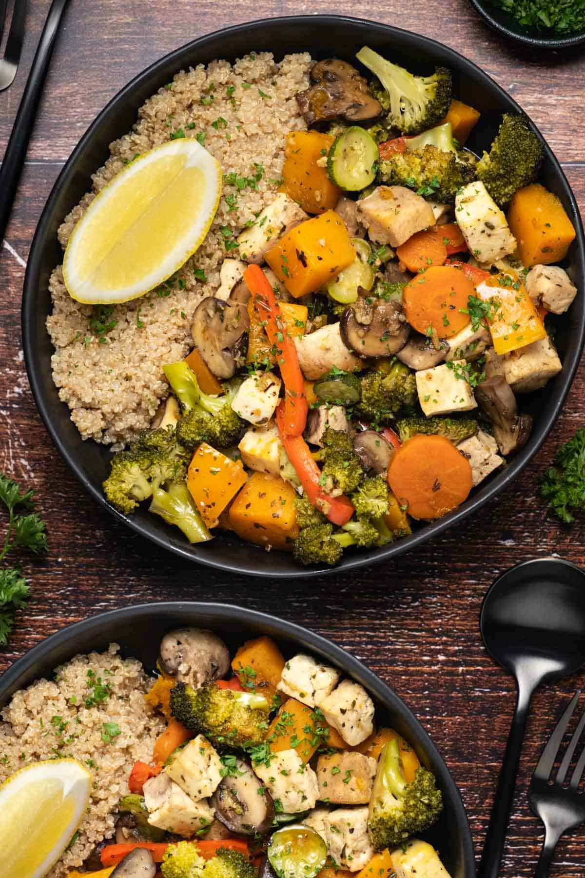 Vegetable casserole with quinoa and lemon wedges in a black bowl. 