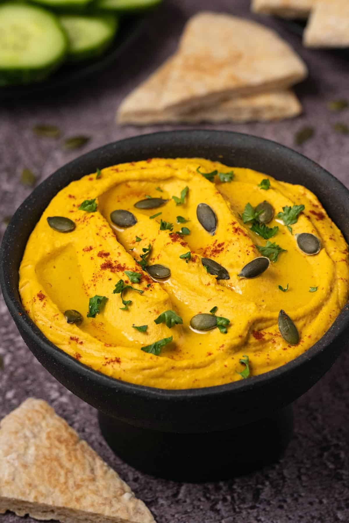Pumpkin hummus topped with fresh parsley and pumpkin seeds in a black bowl. 