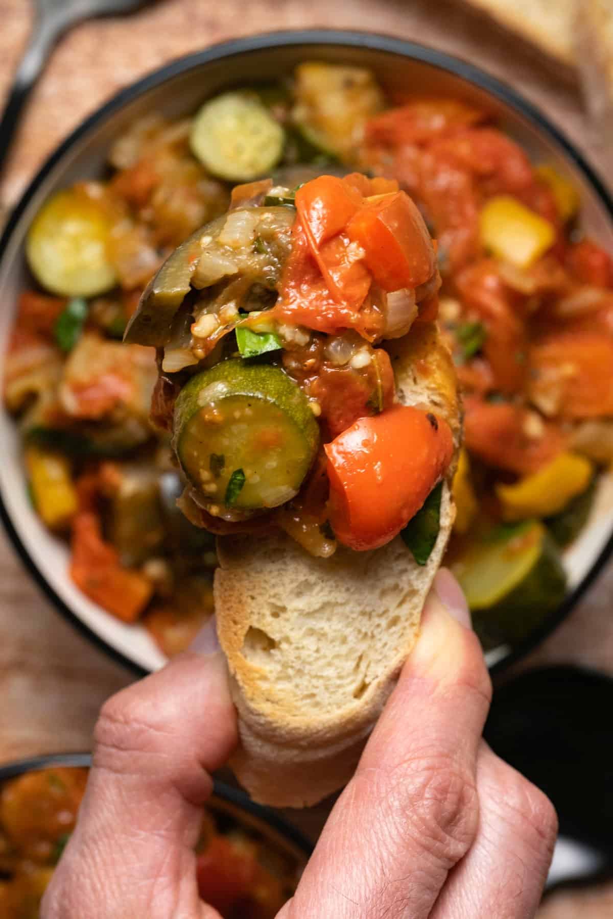 Slice of bread dipping in a bowl of ratatouille. 