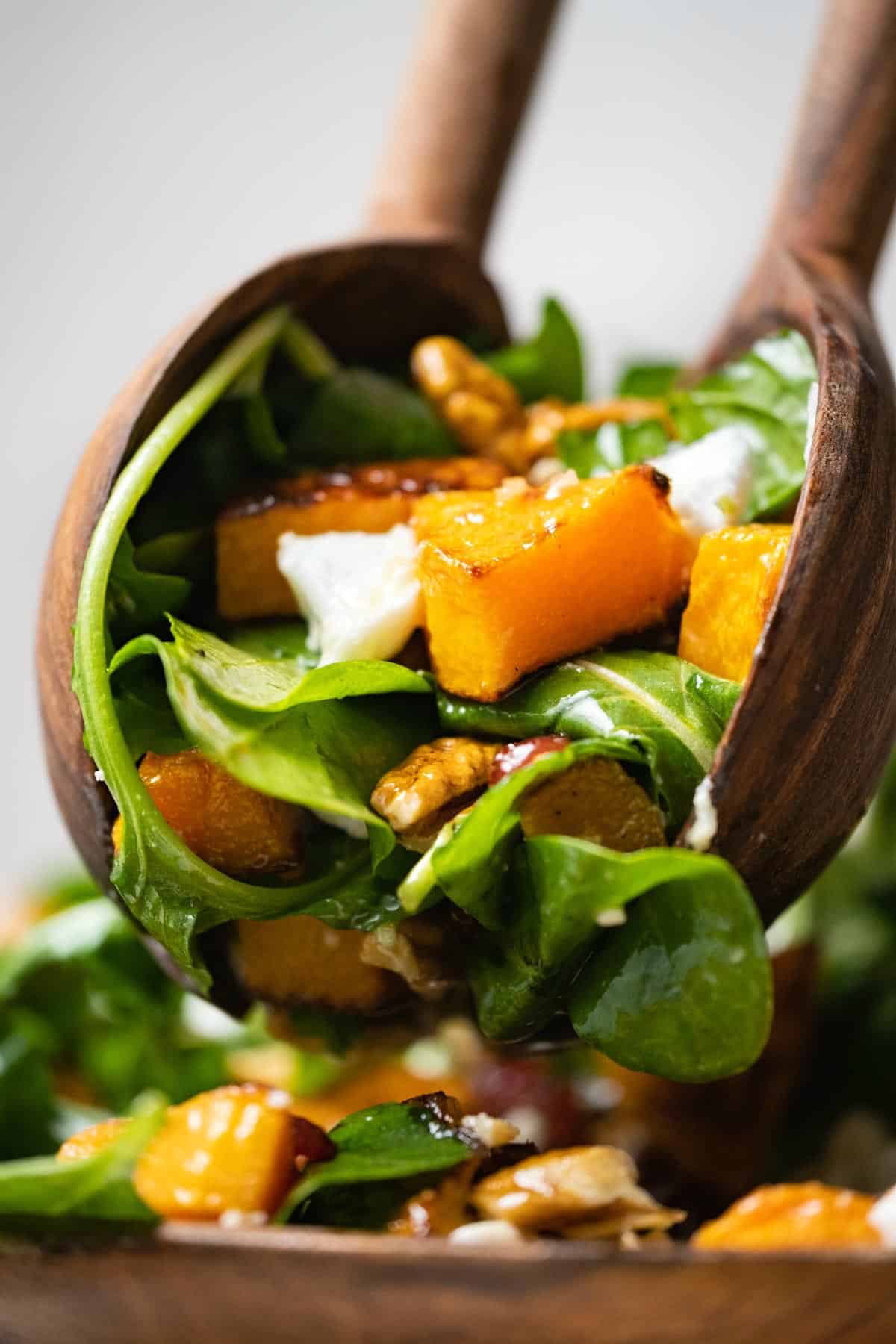 Wooden salad spoons lifting up a serving of butternut squash salad.