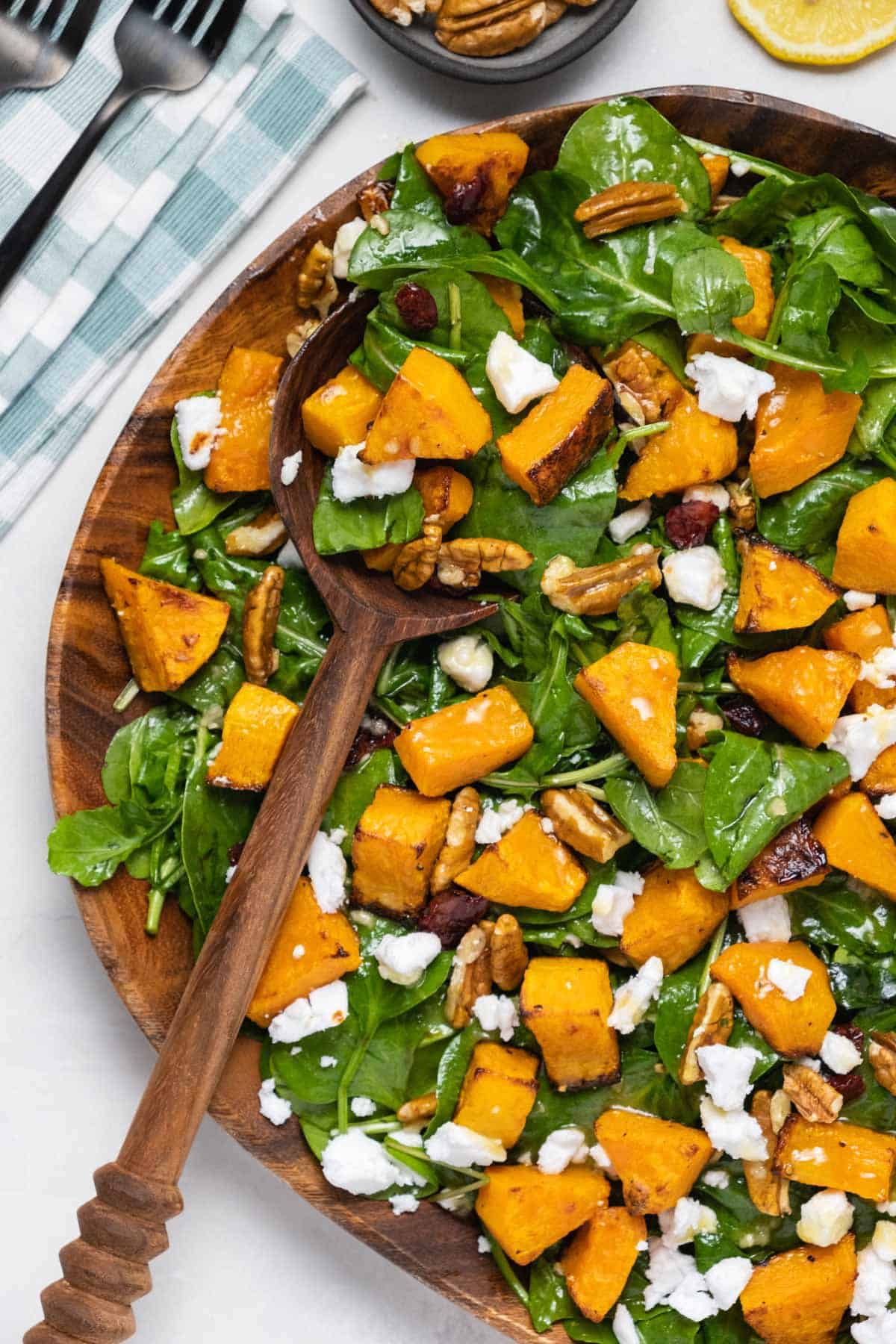 Butternut squash salad in a wooden serving dish with a wooden salad spoon. 