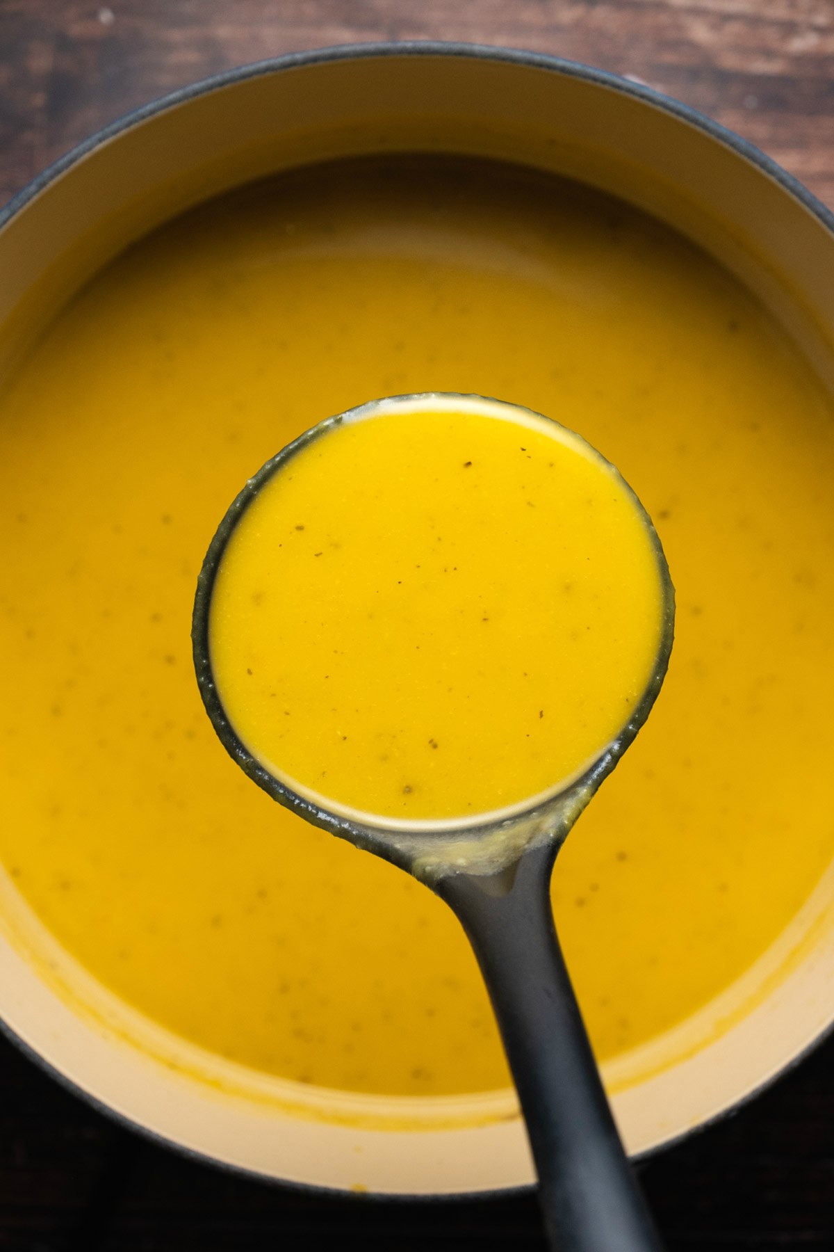 Butternut squash soup in a ceramic pot with a soup ladle. 